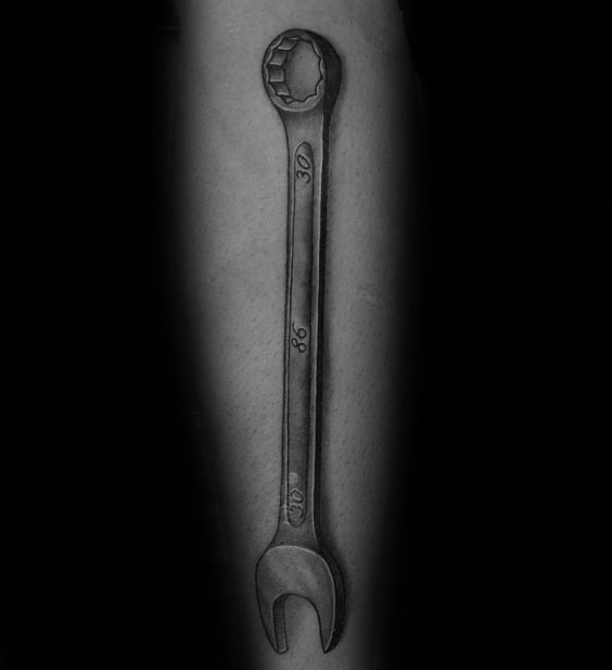 Black and grey tattoo of a long combination wrench on the forearm with engraved numbers 30, 86, and 19 for a personalized touch.