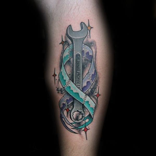Color tattoo of a wrench engraved with "DENNIS MORETTI," wrapped in a blue and purple ribbon with stars and the years '44 and '91, symbolizing remembrance.