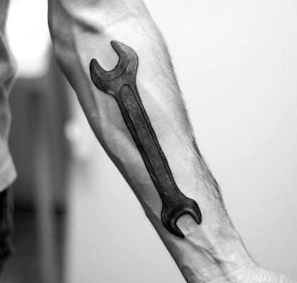 Black and grey tattoo of a double open-end wrench on the forearm, placed along the muscle for a bold and realistic appearance.