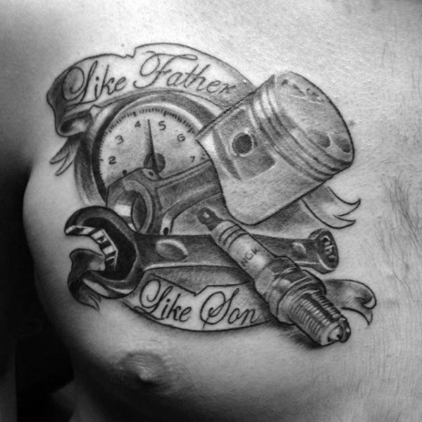 Black and grey chest tattoo featuring a piston, wrench, spark plug, and pressure gauge with a ribbon that reads *Like Father Like Son.*