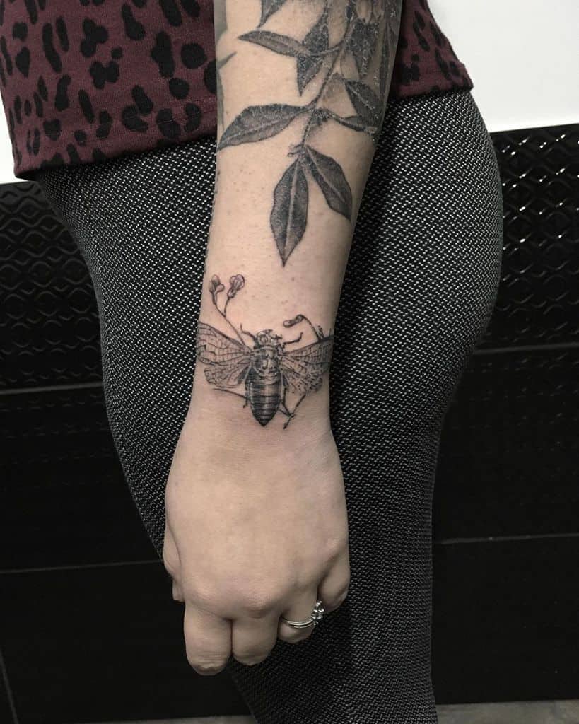 Tattoo of a cicada on a forearm with a leaf tattoo above