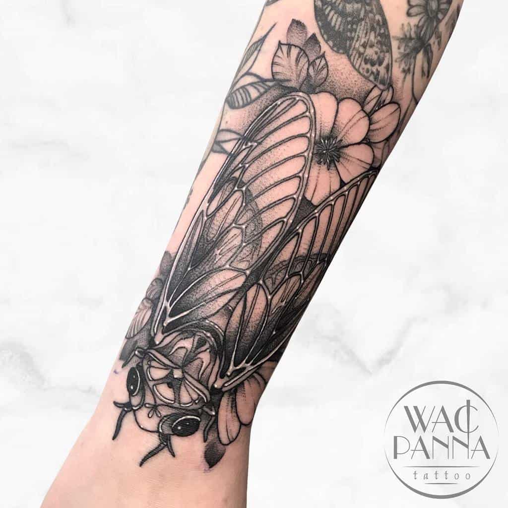 Forearm tattoo of a cicada with floral patterns in black ink