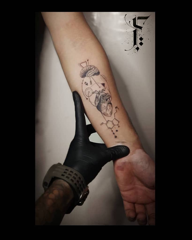 Forearm tattoo of a human heart and brain connected by geometric lines, with serotonin molecule symbols underneath