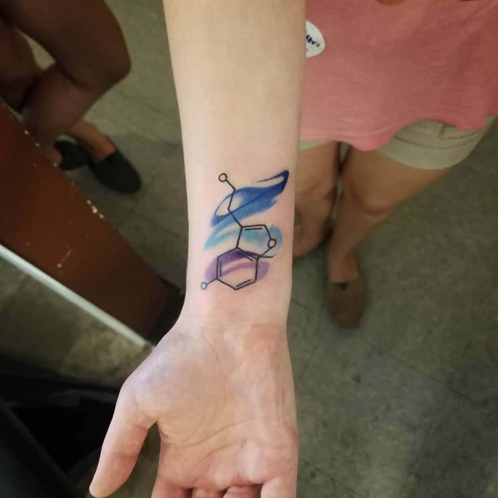 Tattoo of serotonin molecule with blue and purple watercolor on a wrist