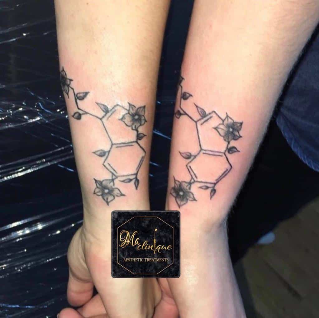 Matching serotonin molecule tattoos on forearms, decorated with small floral accents around the structure