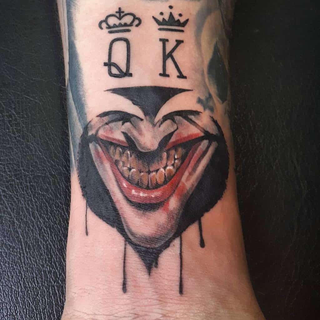A tattoo of a joker's face with a sinister grin in Ace of Spade symbol, featuring the letters "Q" and "K" above it, along with crowns