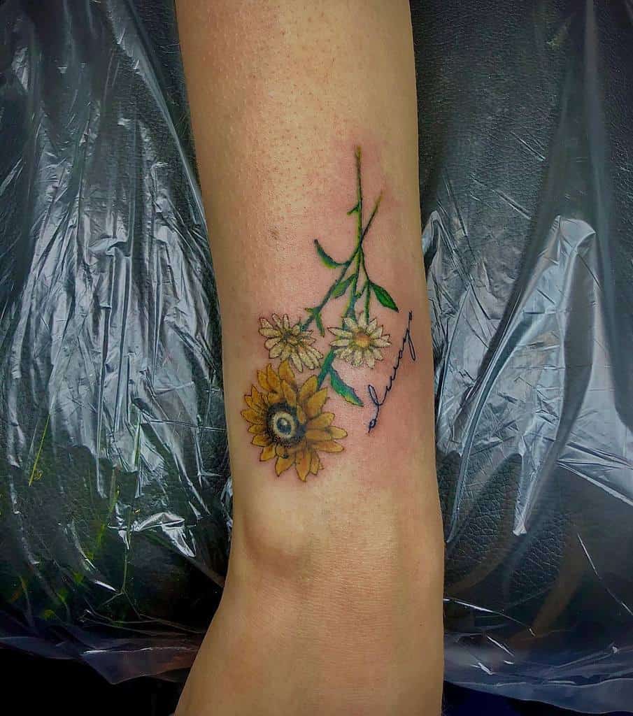 Tattoo of sunflowers and daisies with cursive text "Always" on a forearm