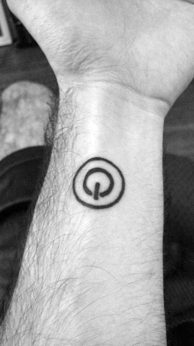 Small power symbol tattoo on the inner wrist, outlined with a double circle for a clean and simple tech-inspired look.