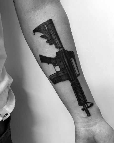 Bold black AR-15 tattoo on the forearm, featuring a solid silhouette design with detailed elements, symbolizing strength, protection, and tactical precision.