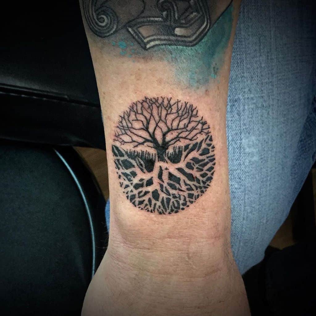 Tattoo of a tree with intricate roots inside a circle on a wrist