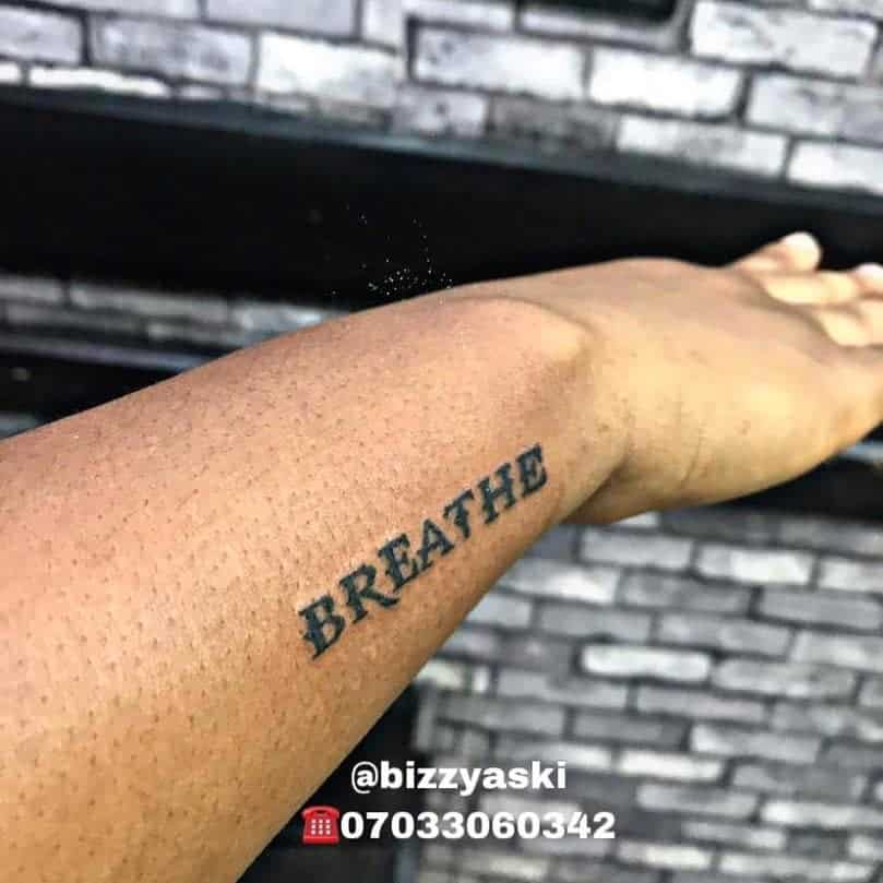 A wrist tattoo boldly displays the word "BREATHE" in striking black ink