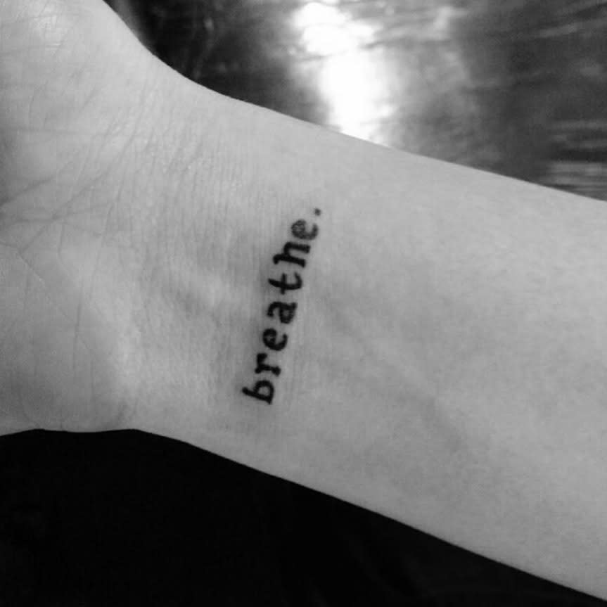 Wrist tattoo elegantly inscribed with the gentle reminder to "breathe"