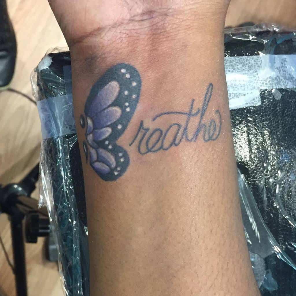 Wrist tattoo of a purple butterfly with the word "breathe" written beside it
