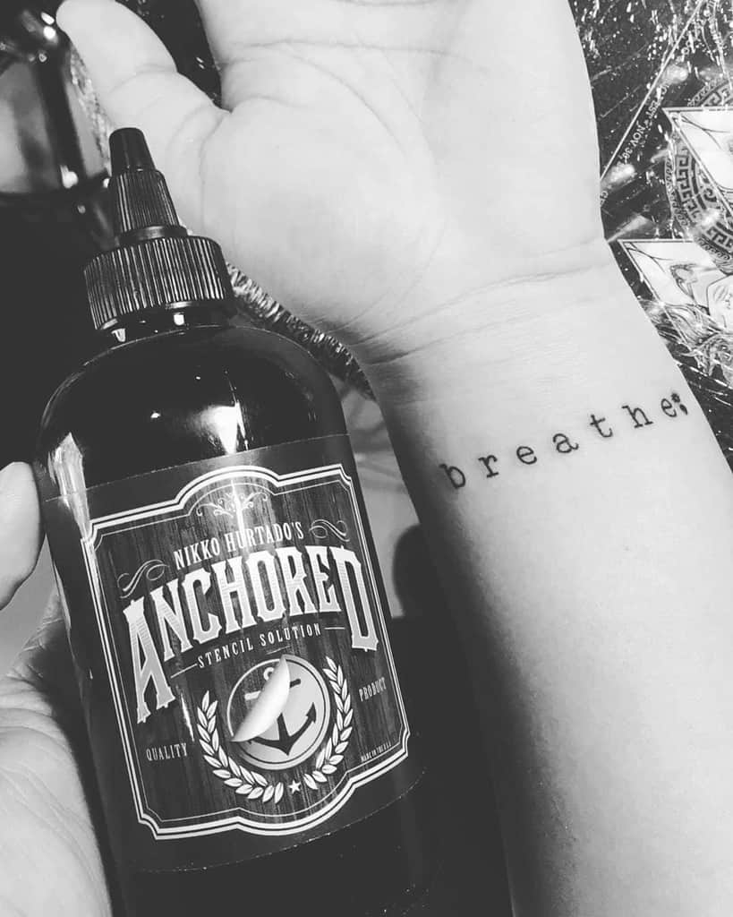 Wrist tattoo that reads "breathe;"