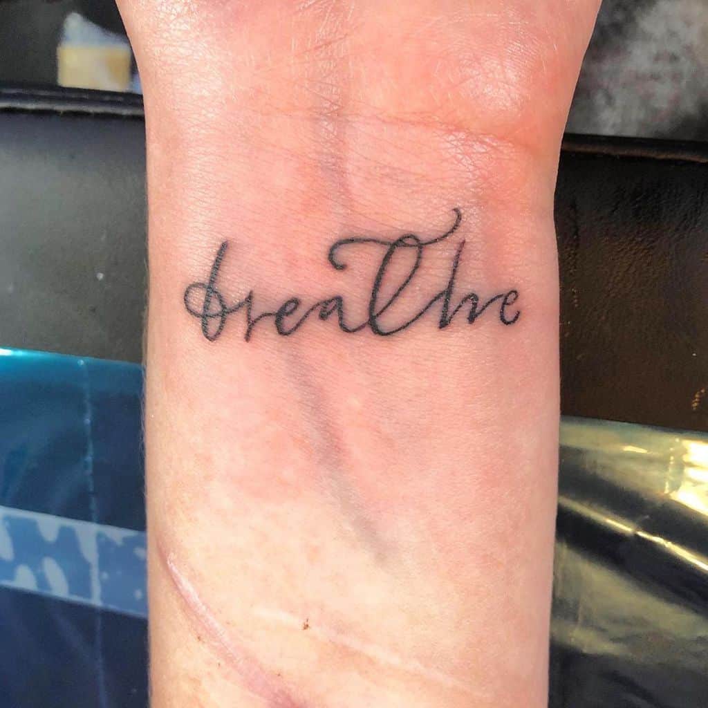 A wrist tattoo with the word "breathe" in cursive script