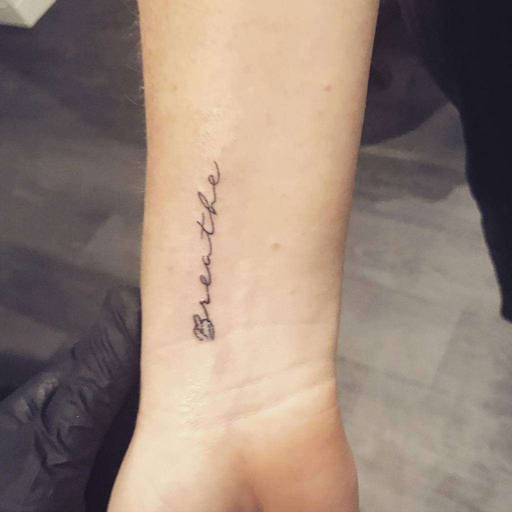 Tattoo on wrist reading "breathe" in cursive script