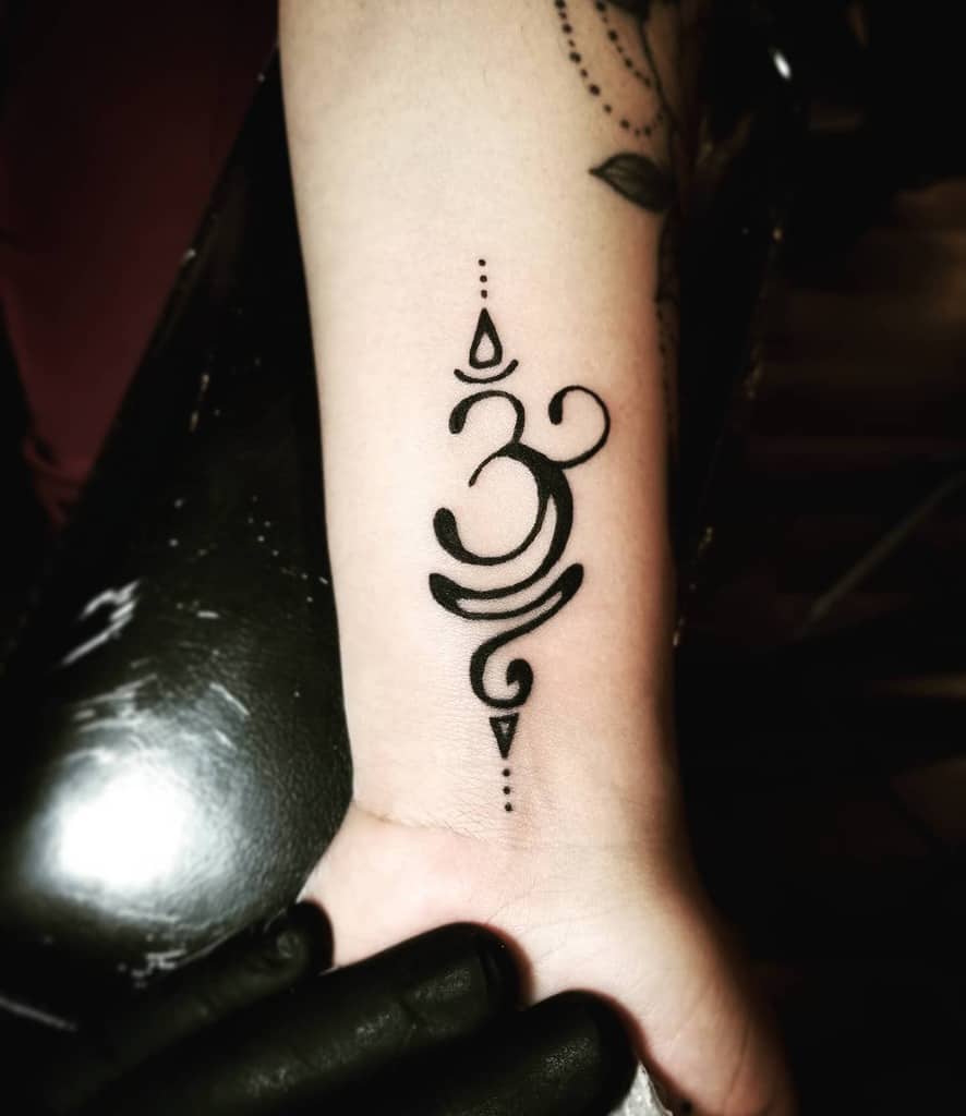 A black Om symbol tattoo with decorative elements on a wrist