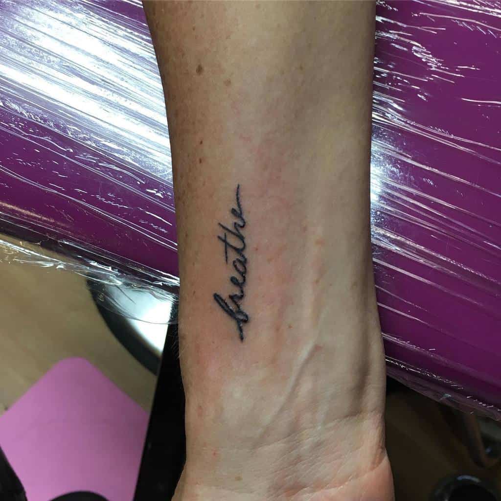 Simple wrist tattoo of the word 'breathe' in delicate cursive font, inked in fine black lines