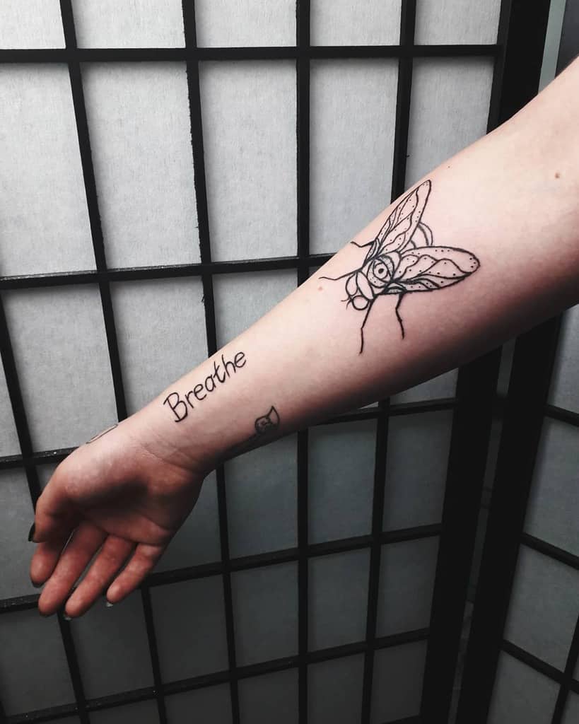 Arm tattoo with an intricate fly and the word "Breathe" written below