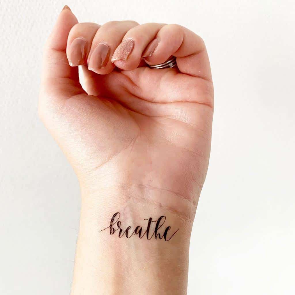 A hand with a tattoo on the wrist that reads "breathe"