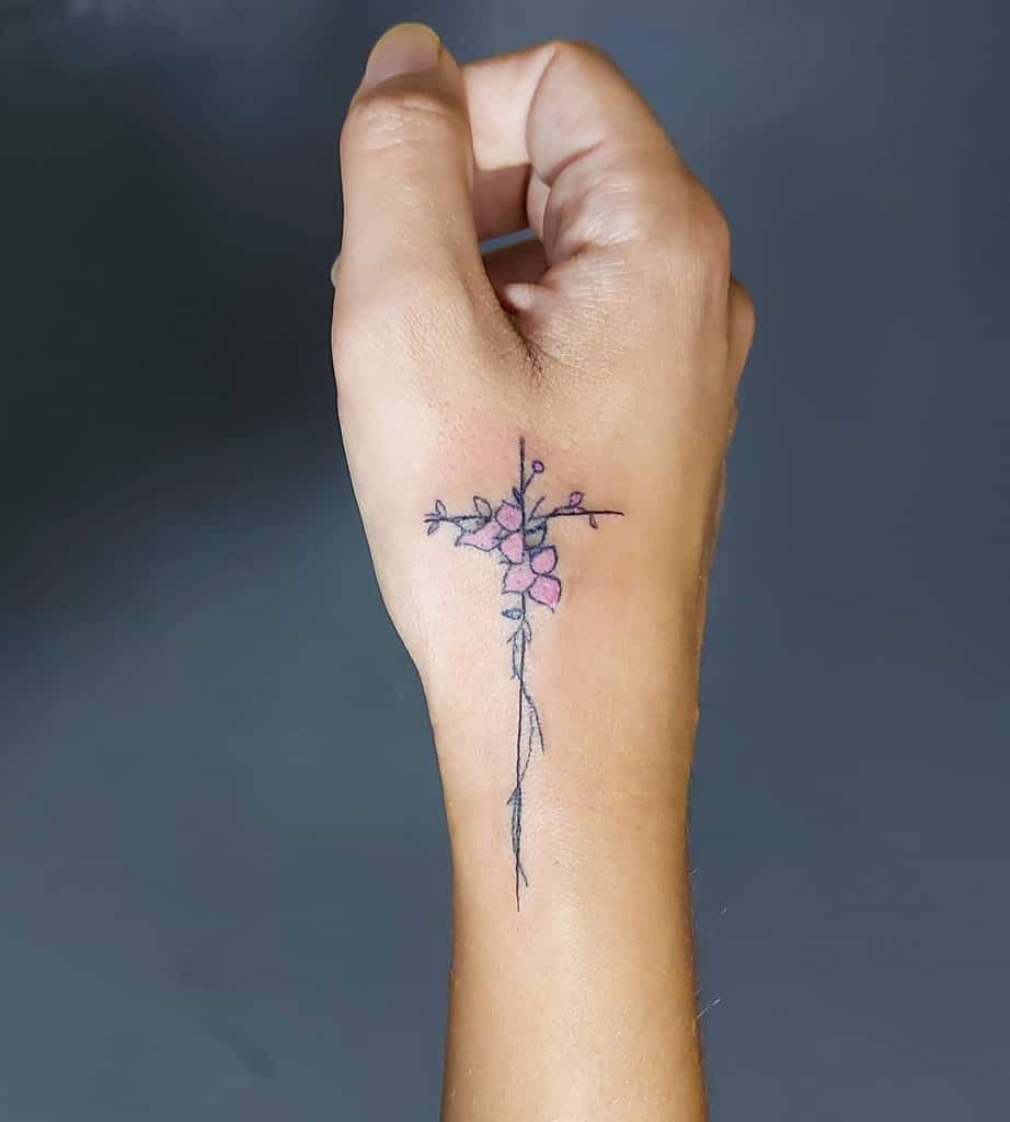 Minimalist floral tattoo on the back of a hand with delicate pink flowers arranged in a cross shape