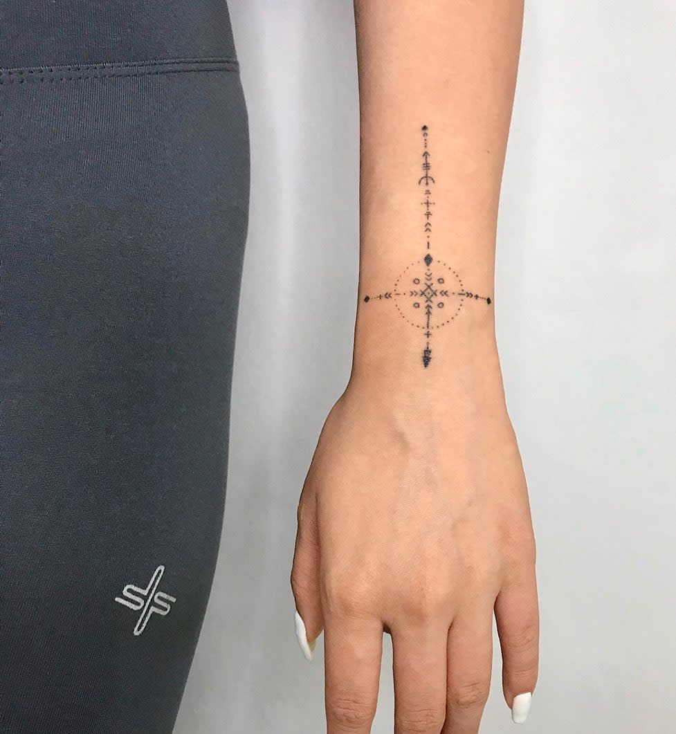 A geometric wrist tattoo featuring a symmetrical cross made up of intricate dotted lines and small decorative elements, creating a modern and detailed design
