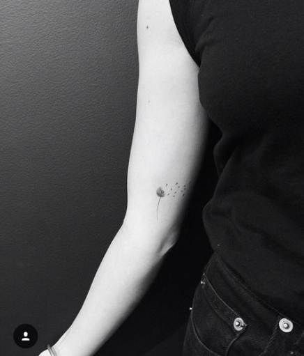 Small dandelion tattoo on the inner arm with seeds floating away, symbolizing hope, change, and new beginnings.