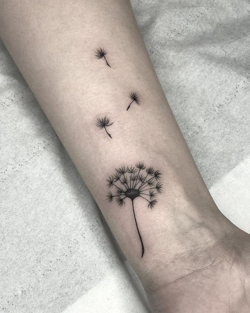 Minimalist dandelion tattoo on the forearm with seeds drifting away, symbolizing wishes, hope, and new beginnings.