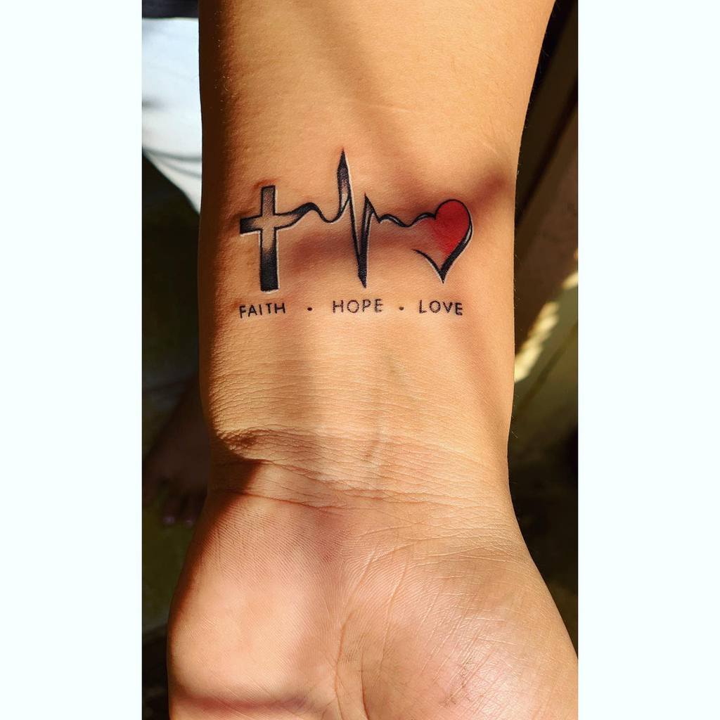 Wrist tattoo featuring a cross, heartbeat line, and heart with the text "FAITH HOPE LOVE" below each symbol