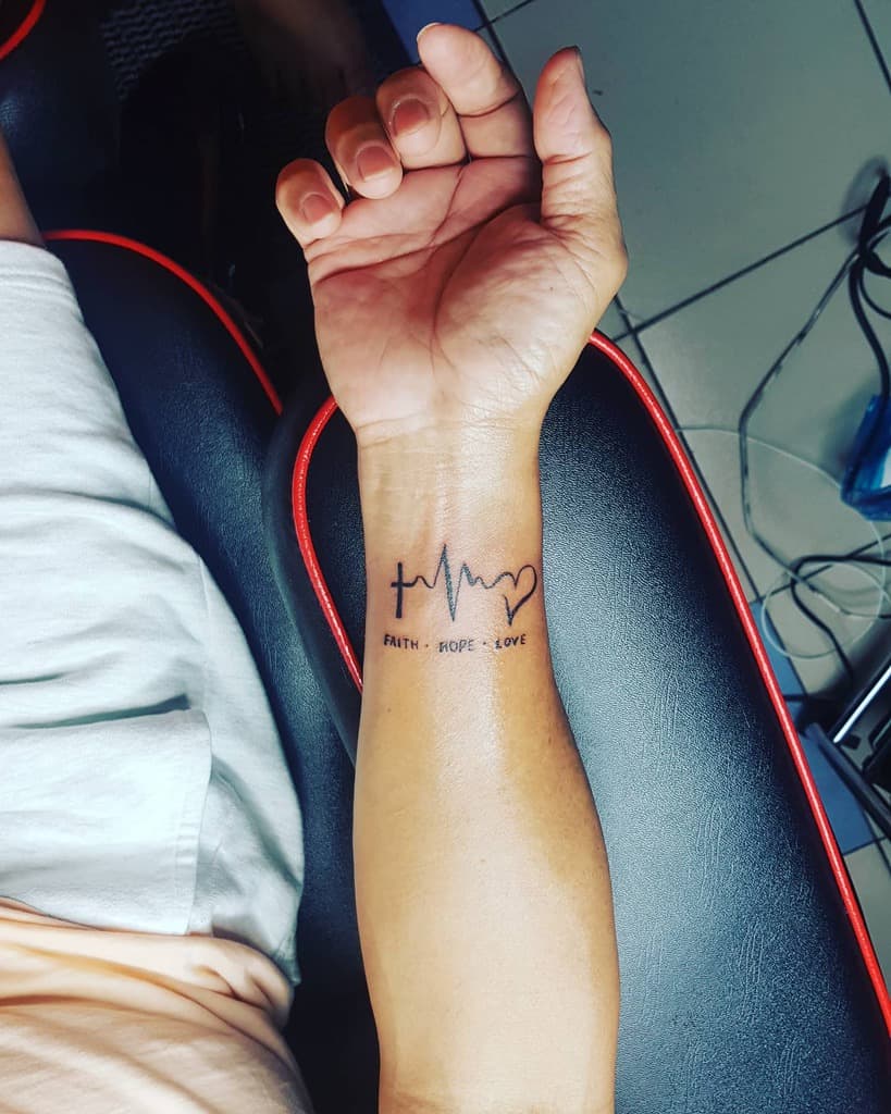 Wrist tattoo of a heartbeat line with "faith + hope + love" text