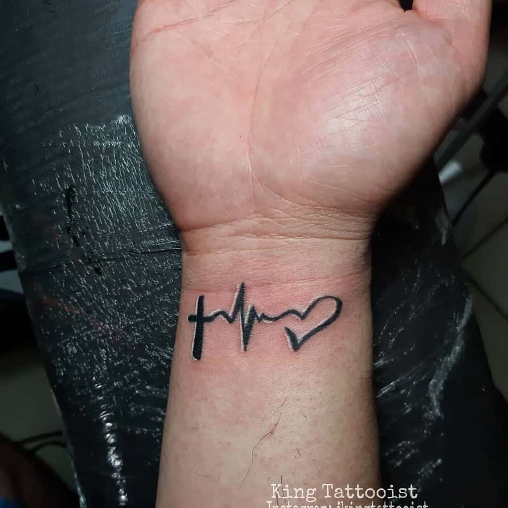 A wrist tattoo featuring a cross, a heartbeat line, and a heart symbol, representing faith, hope, and love, done in a bold black ink style