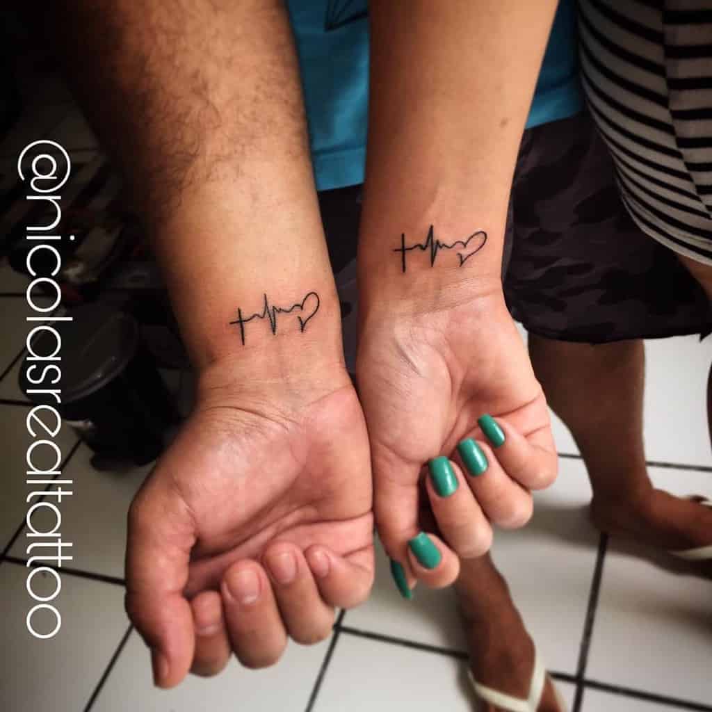 Matching wrist tattoos on two people, featuring the symbols for faith, hope, and love: a cross, heartbeat line, and a heart, inked in black