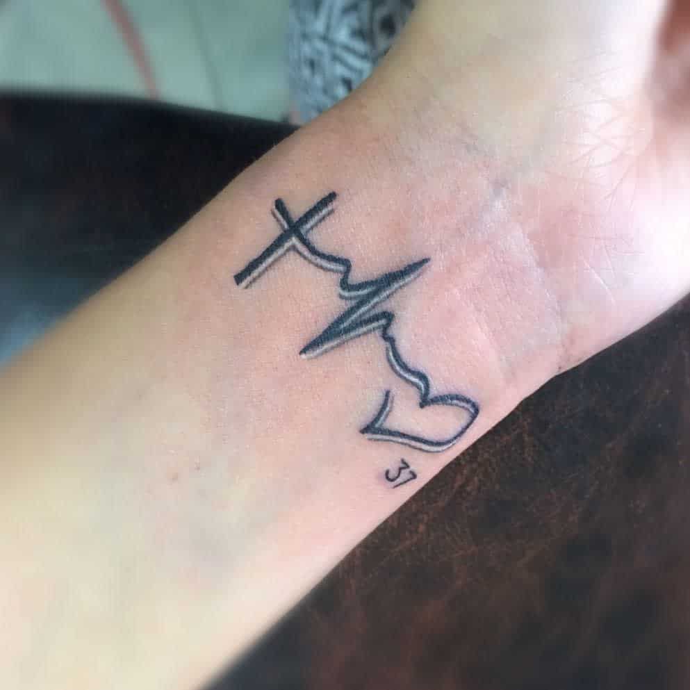 Tattoo on a wrist showing a cross, heartbeat line, heart, and the number 37