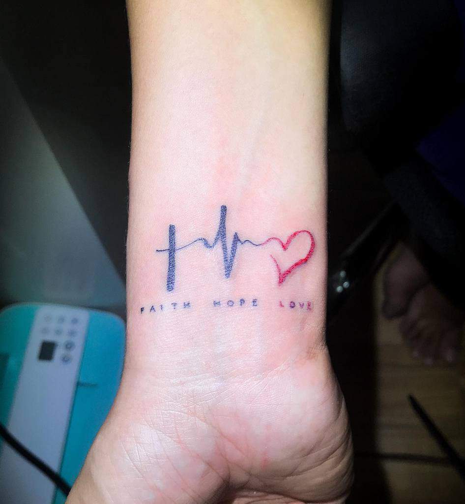 Wrist tattoo showing a cross, heartbeat line, and heart with the words "Faith Hope Love" below