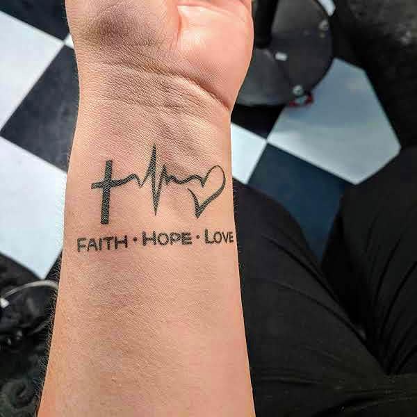 Wrist tattoo with cross, heartbeat line, heart, and text "FAITH HOPE LOVE"