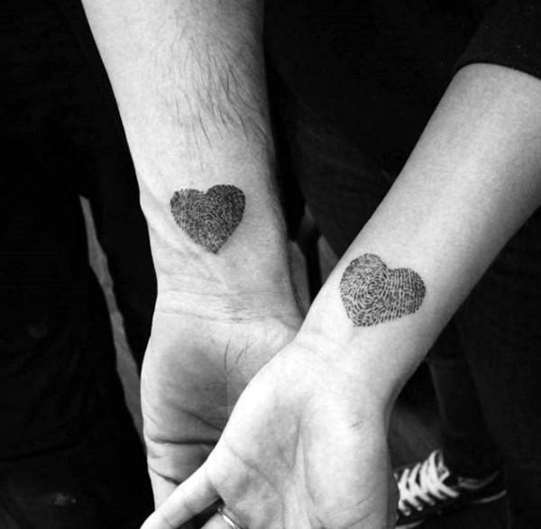 Matching wrist tattoos of heart shapes filled with fingerprint patterns, symbolizing a unique and personal love that leaves a lasting mark.