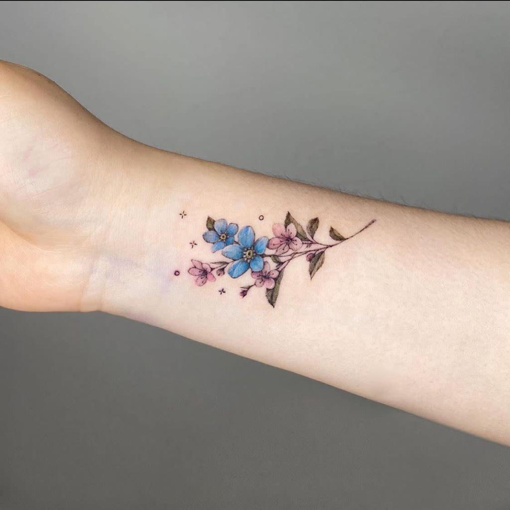 A charming tattoo of blue and pink forget-me-nots, accompanied by small star-like accents, delicately placed on the inner wrist