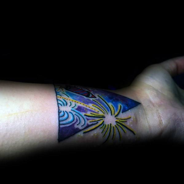 Tattoo of a vibrant firework explosion wrapping around the wrist, featuring bold yellow and blue bursts with dynamic shading for a striking effect.