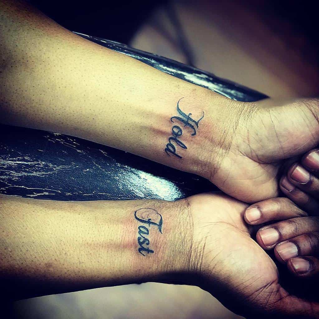 Two wrists with tattoos reading "Hold" and "Fast" in cursive script