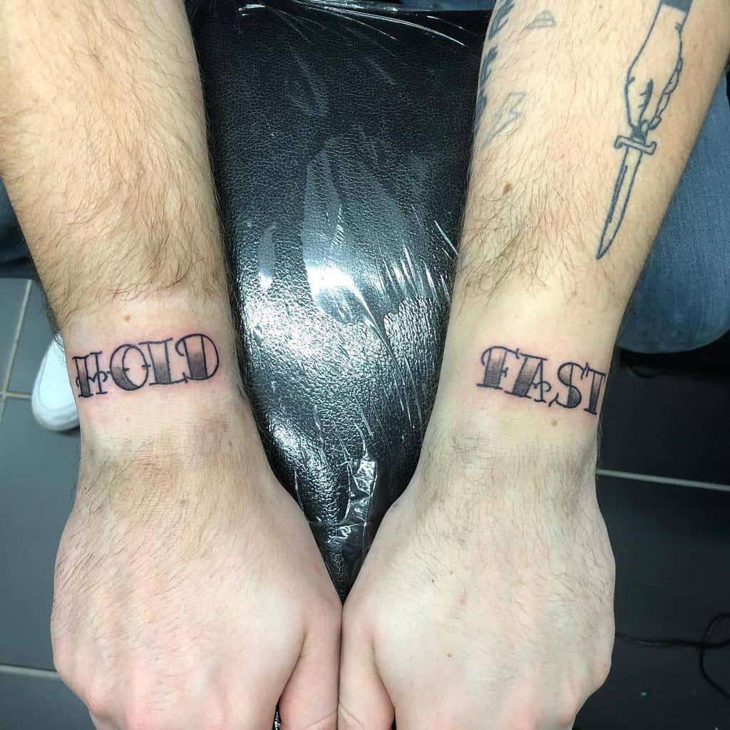 Forearms with "HOLD" and "FAST" tattoos on wrists, and a dagger tattoo on left arm