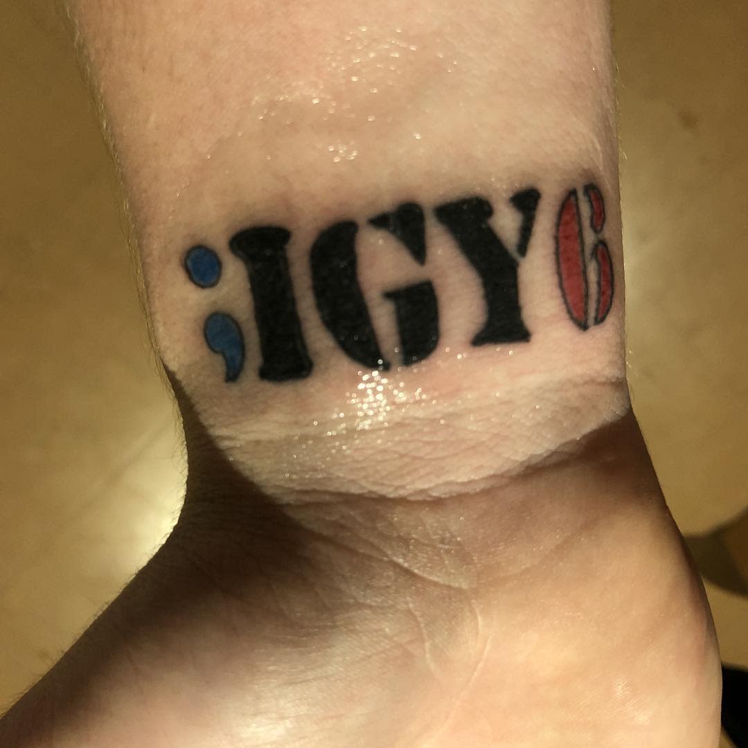 Tattoo on wrist reading ";IGY6" with a red and blue semicolon symbol