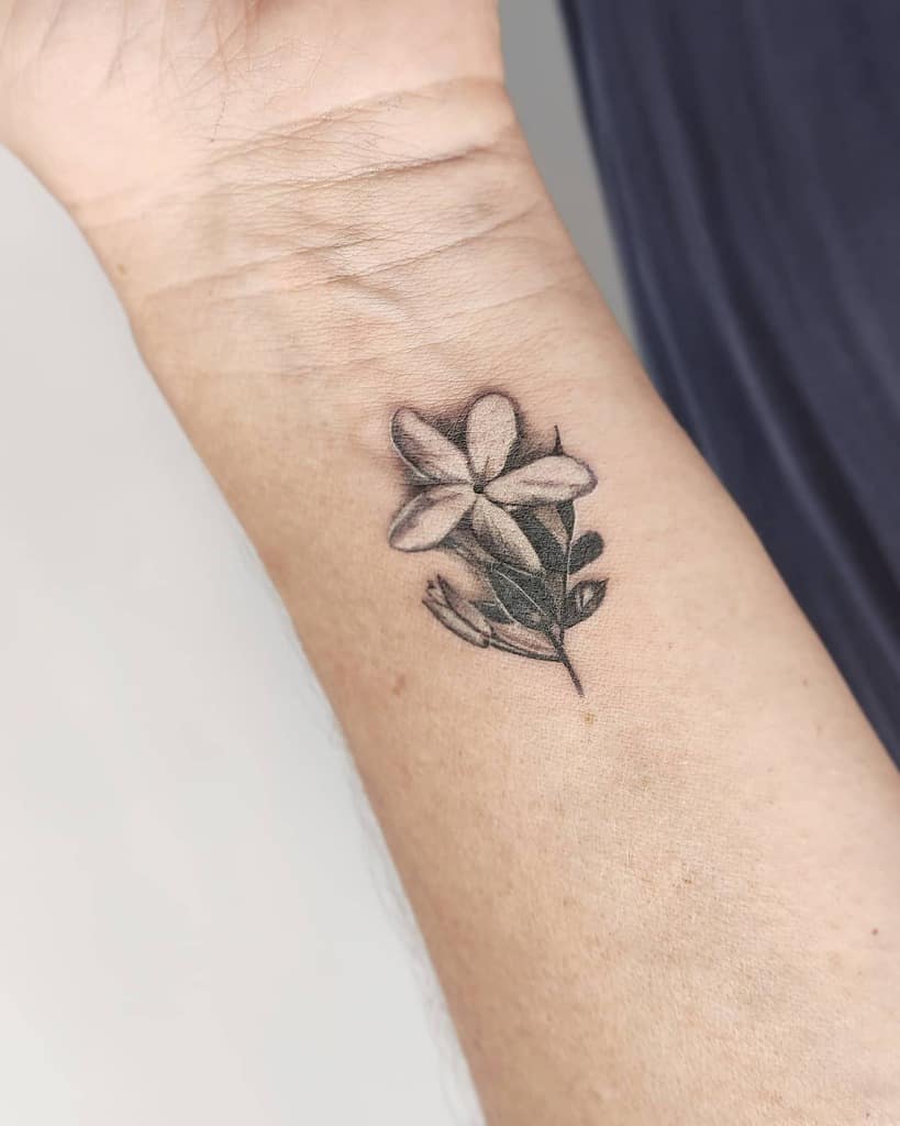 Forearm tattoo of a jasmine flower with three petals and a few leaves, located near the wrist