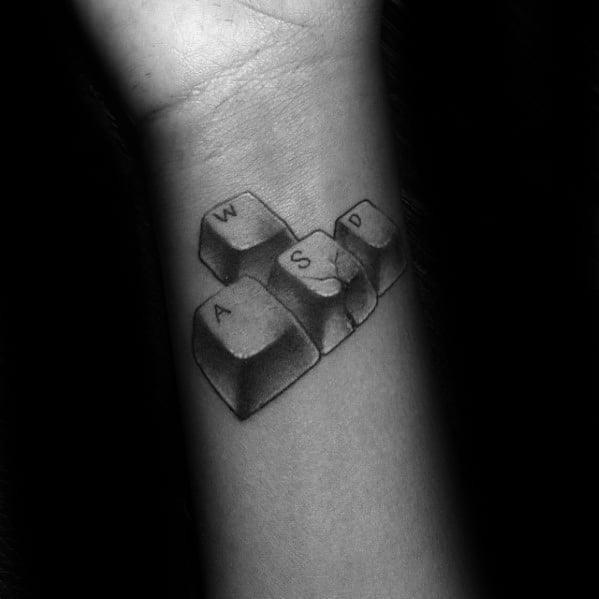 Realistic black and grey tattoo of the W, A, S, and D keyboard keys, commonly used in gaming, placed on the inner wrist.