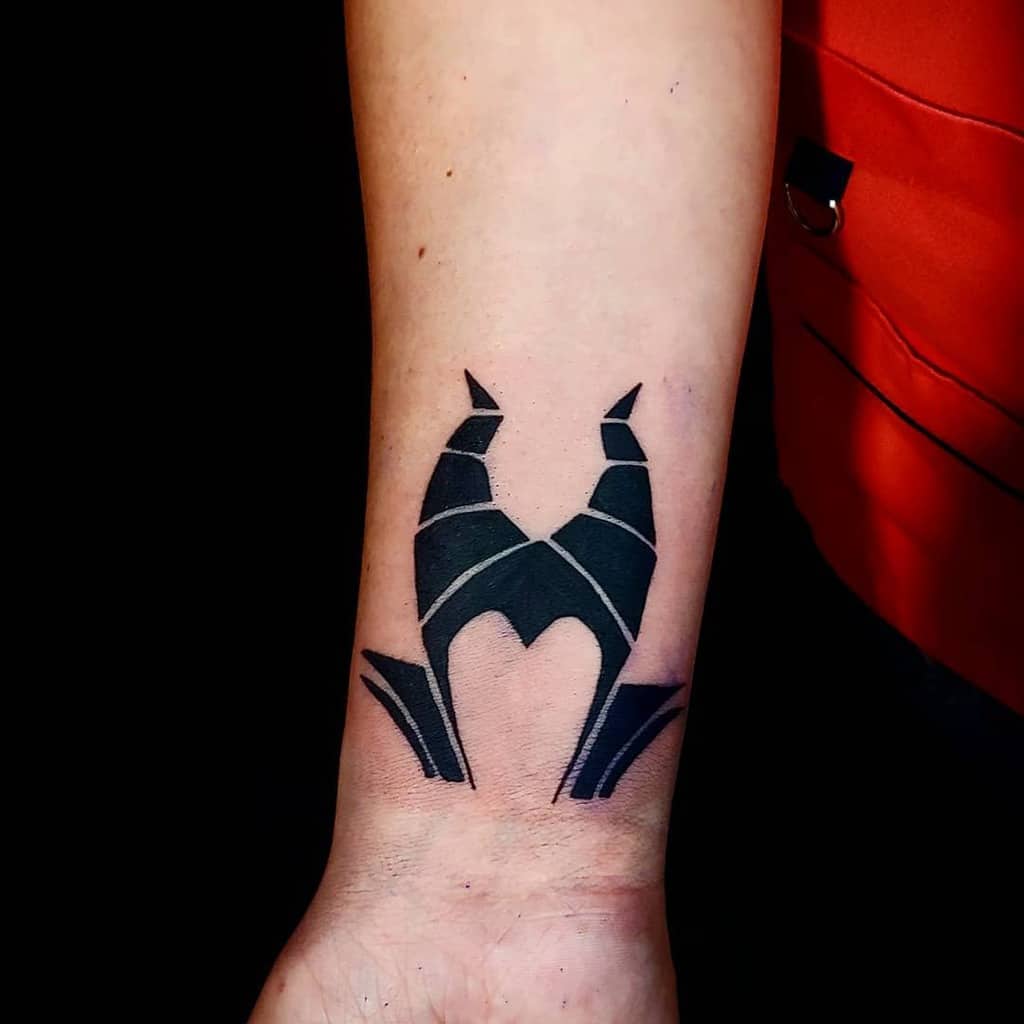 Maleficent-themed black and gray abstract tattoo on a forearm