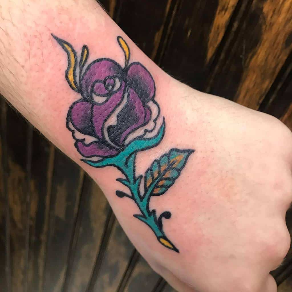 Tattoo of a purple rose with a green stem and leaf on a forearm