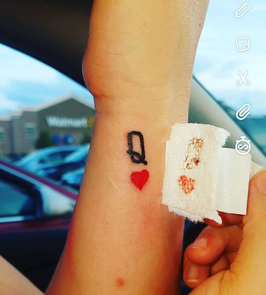 Tattoo of a black letter "Q" and red heart on a wrist