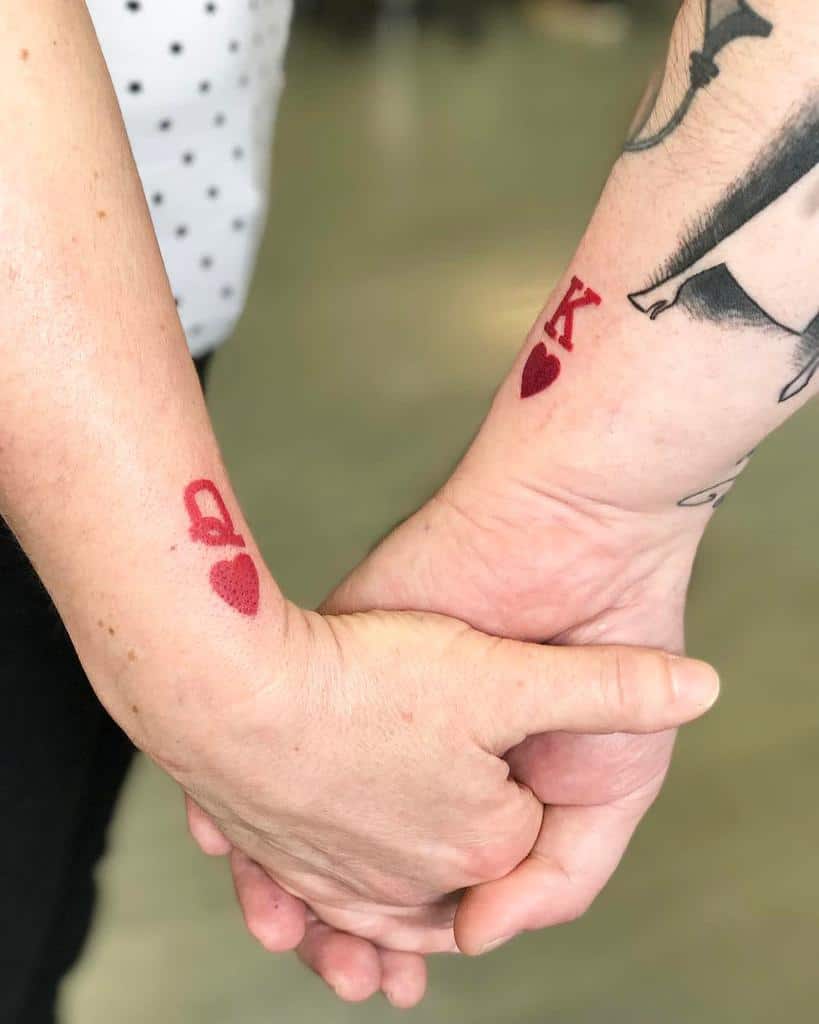 Two people holding hands with red heart tattoos, one marked "Q" and the other "K"