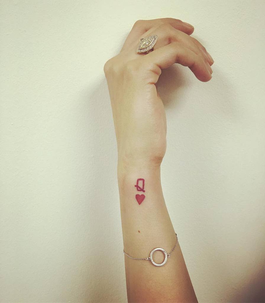 Wrist tattoo with a red heart and queen of hearts symbol on a woman's arm