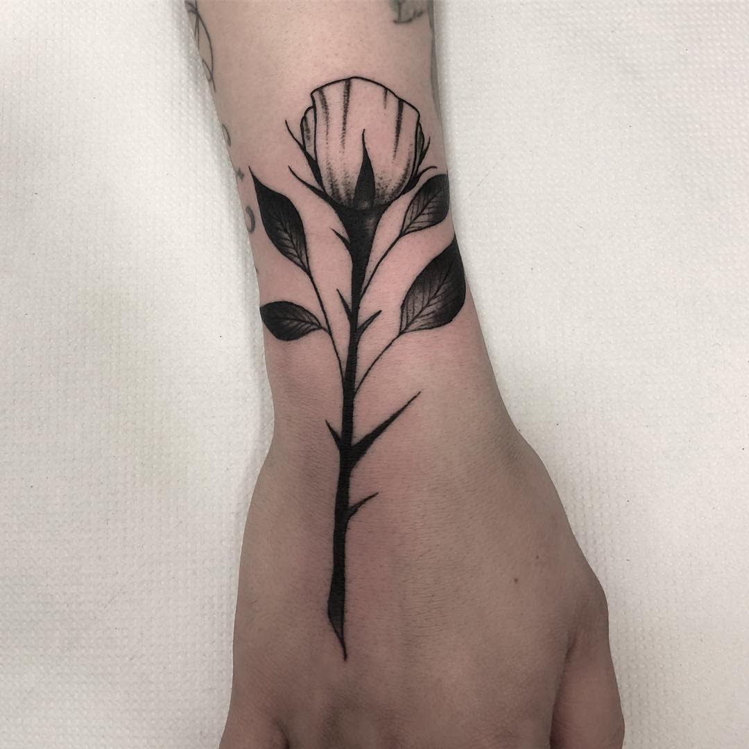 Minimalist black floral tattoo with a delicate stem gracing a person's arm