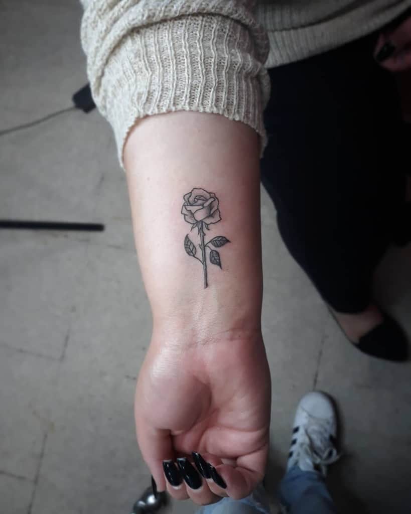 Minimalistic wrist tattoo of a single rose with a delicate stem and leaves, symbolizing elegance and simplicity